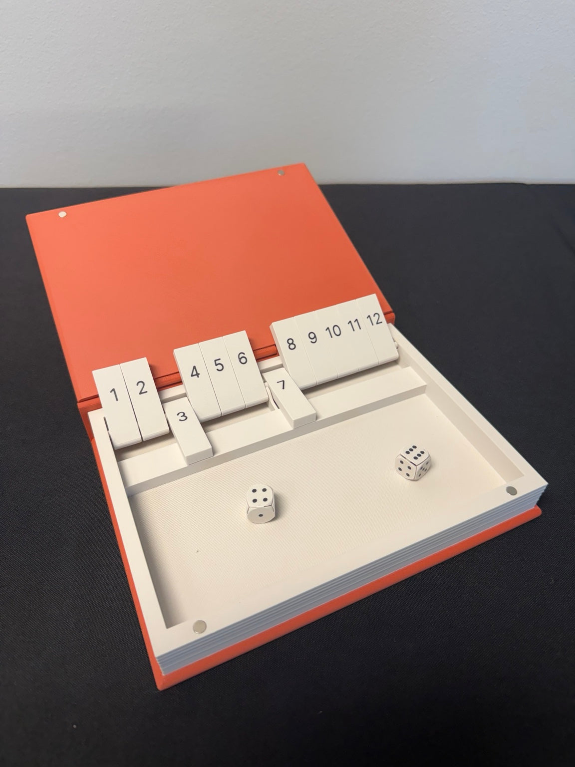 Open orange Shut the Box book game with numbered tiles and dice