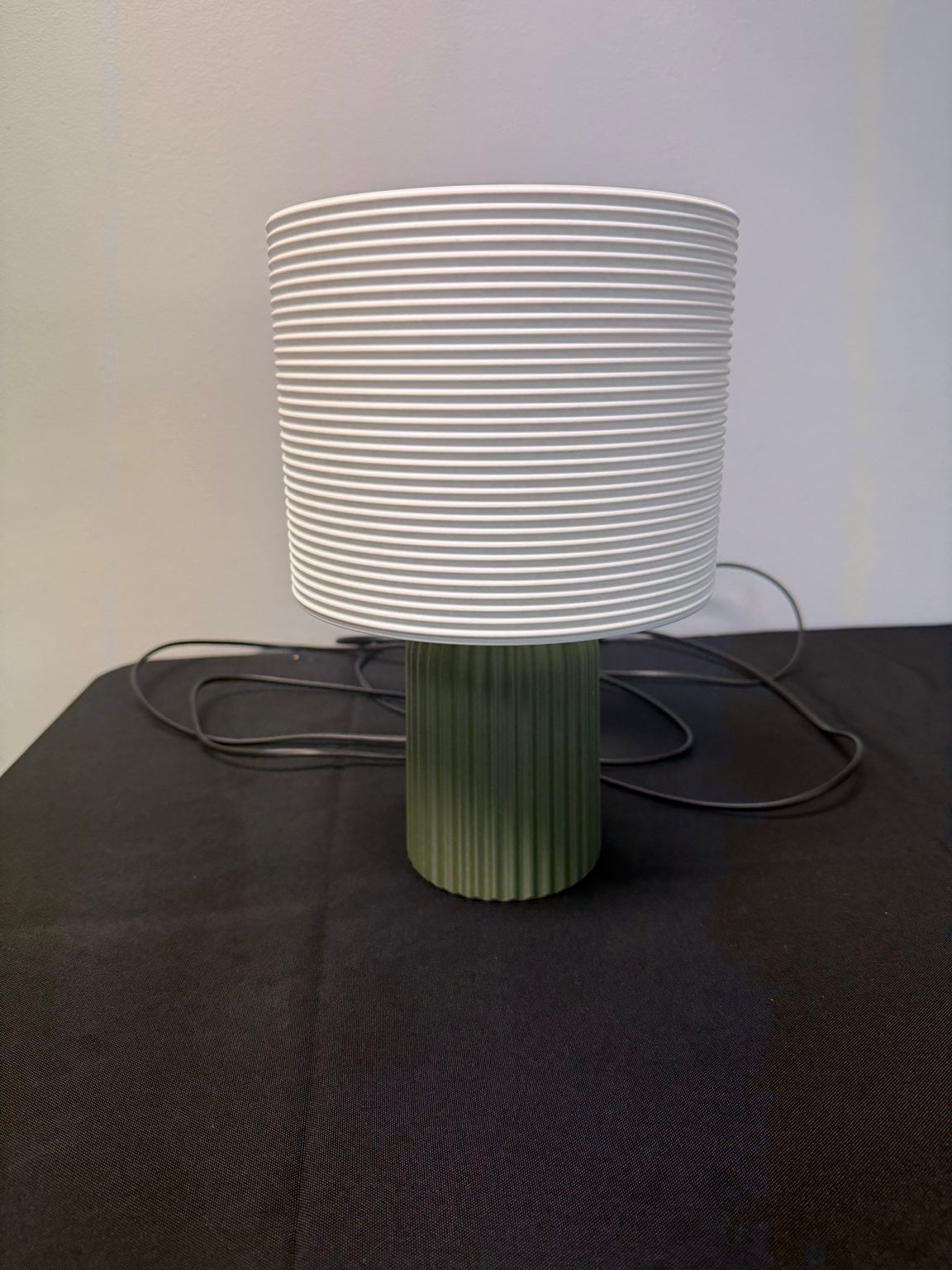 Ribbed cream lampshade on a green ribbed base with its cord